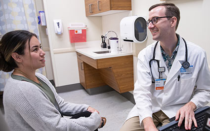 Patient speaking with doctor in white coat sitting at a computer.