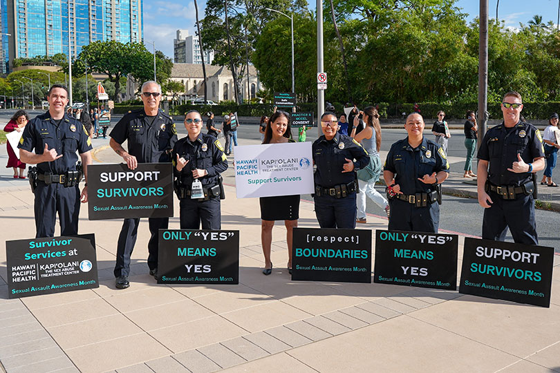 Community leaders and Honolulu police offers with signs promoting sexual assault awareness.