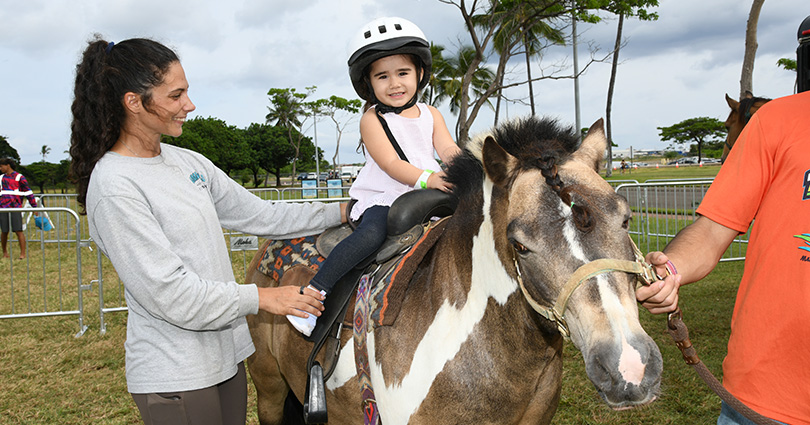 Young girl wearing a helpmet riding a horse being lead by handlers.