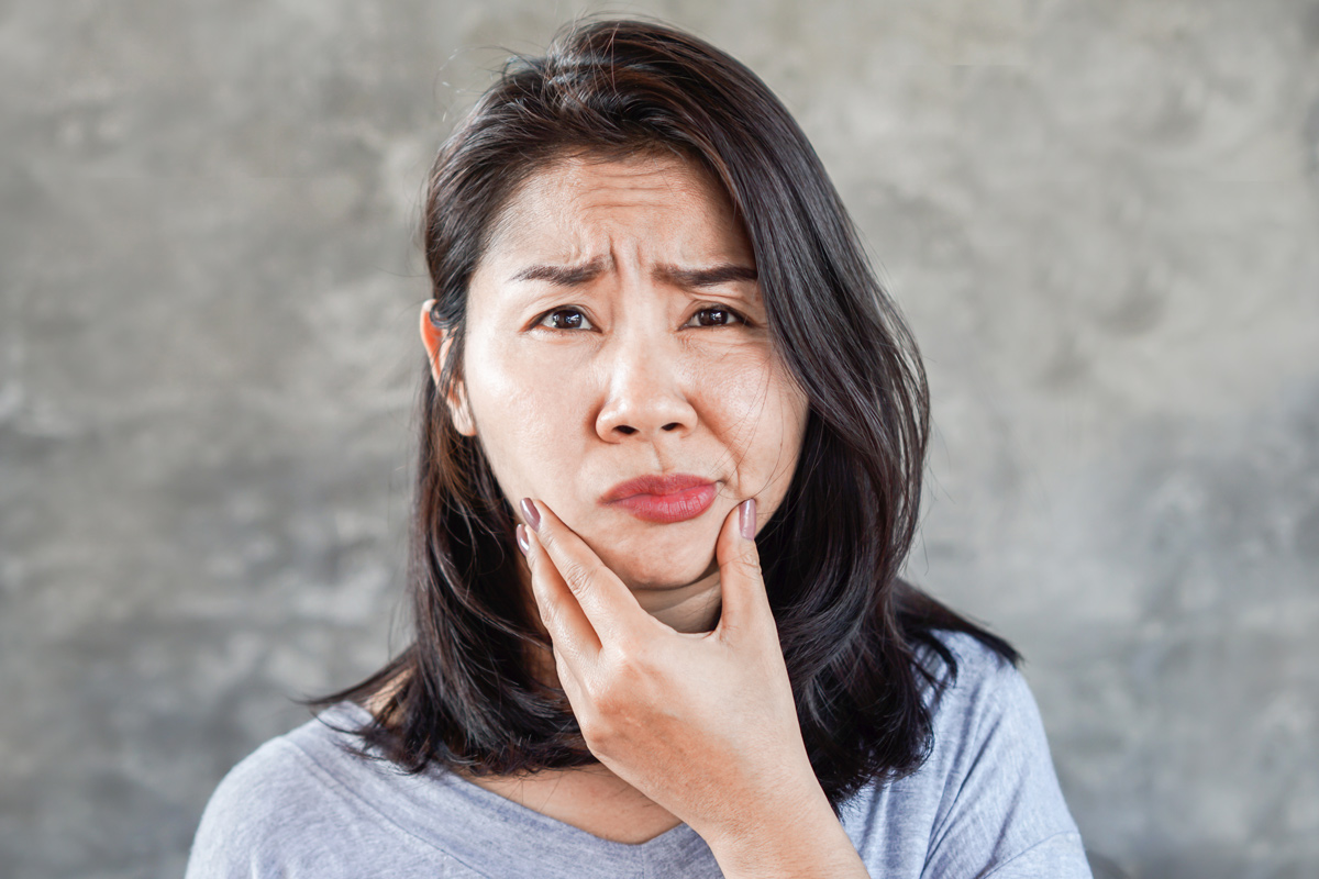 a middle-age Asian woman holds her chin as her face droops to one side indicating a stroke