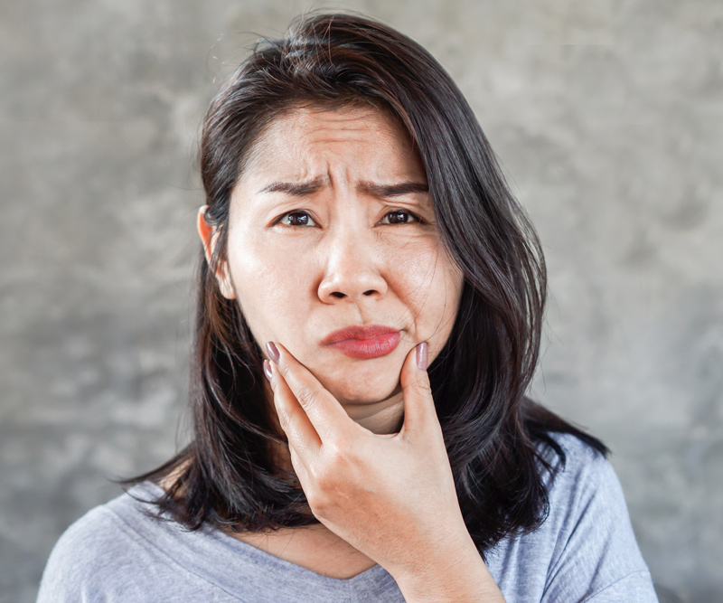 a middle-age Asian woman holds her chin as her face droops to one side indicating a stroke