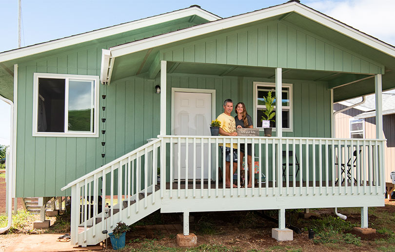 Couple standing in front of their new sage green home.