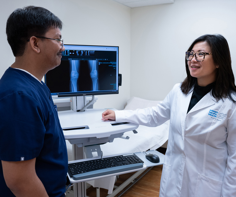 a male medical assistant and female doctor review an X-ray of a knee in an exam room