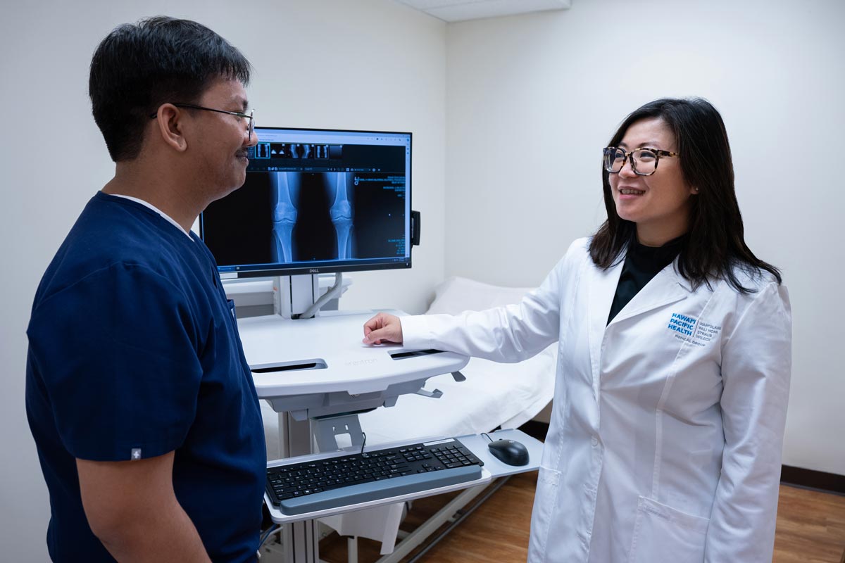 a male medical assistant and female doctor review an X-ray of a knee in an exam room