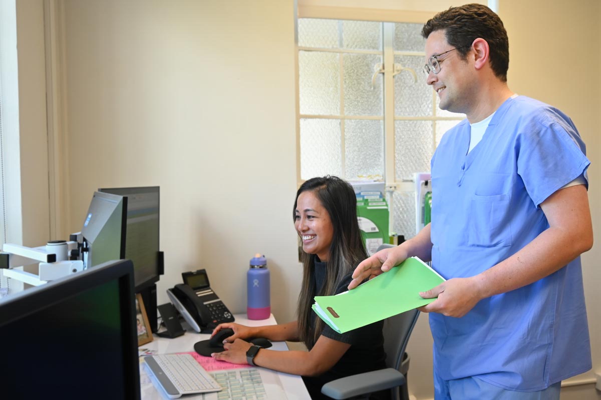 A doctor stands and looks at a computer with a program coordinator who is seated in front of the screen