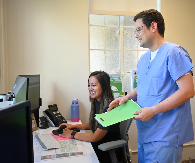 A doctor stands and looks at a computer with a program coordinator who is seated in front of the screen