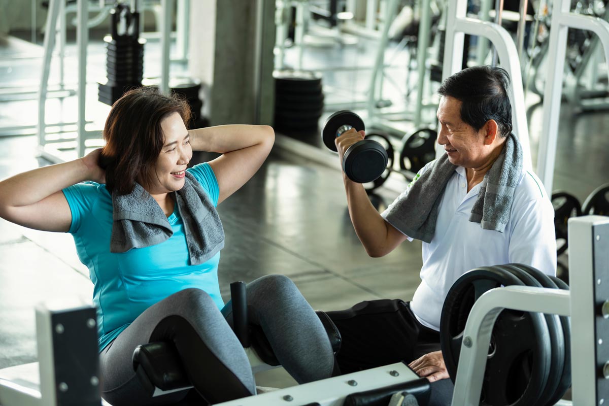 An older woman and man lift weights together in a gym