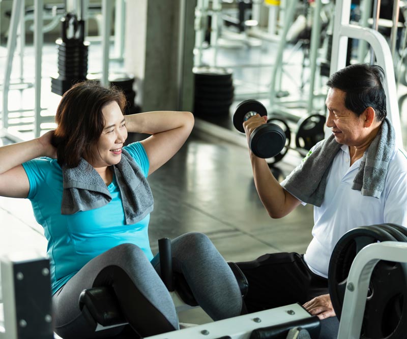 An older woman and man lift weights together in a gym