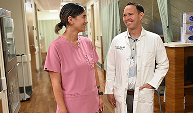 Two medical care providers in a clinic hallway having a friendly discussion.