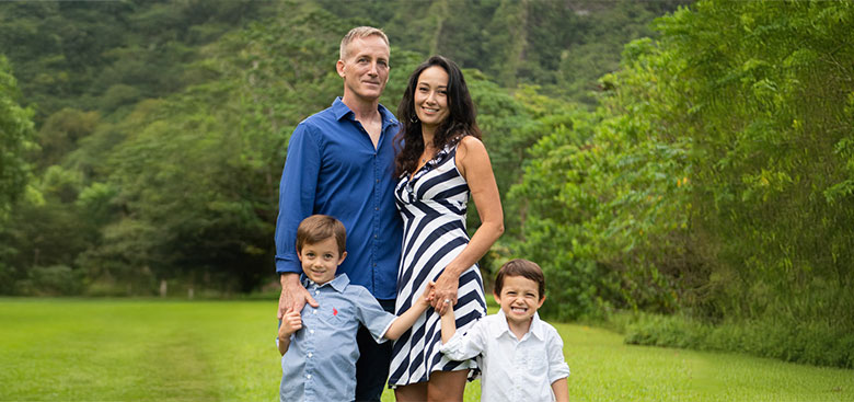 Portrait of a family of four standing together outside with greenery all around.