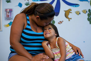 Mother with her arm around her young smiling daughter.