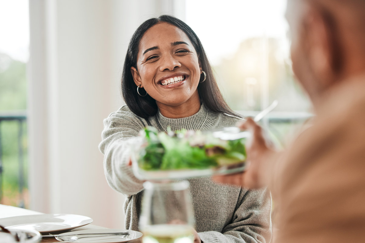 woman smiles and passes the salad plate at a holiday dinner