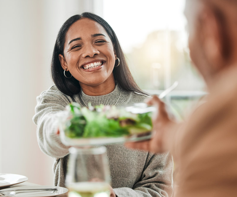 woman smiles and passes the salad plate at a holiday dinner