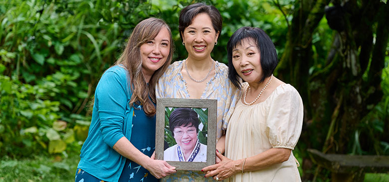 Three smiling women with hands on a loving portrait photo of a fourth.