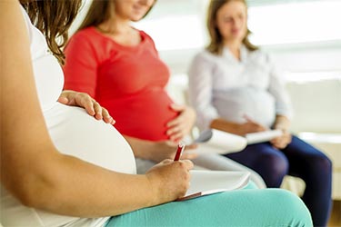 Pregnant women sitting together one in foreground taking notes.