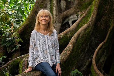 Smiling woman sitting on the roots of a very large tree.