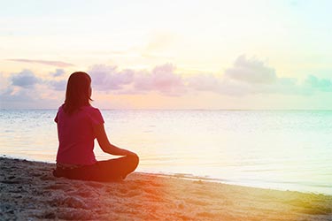 Silhouette of woman sitting cross legged on the beach at sunrise.