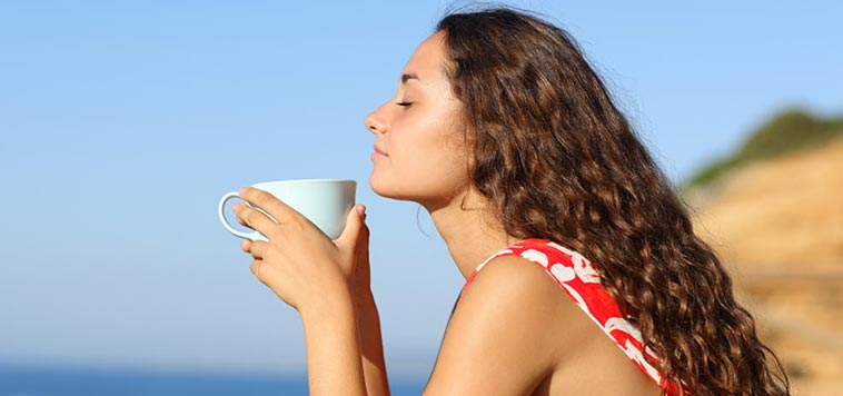 Woman with eyes closed enjoying a cup of tea by the ocean.