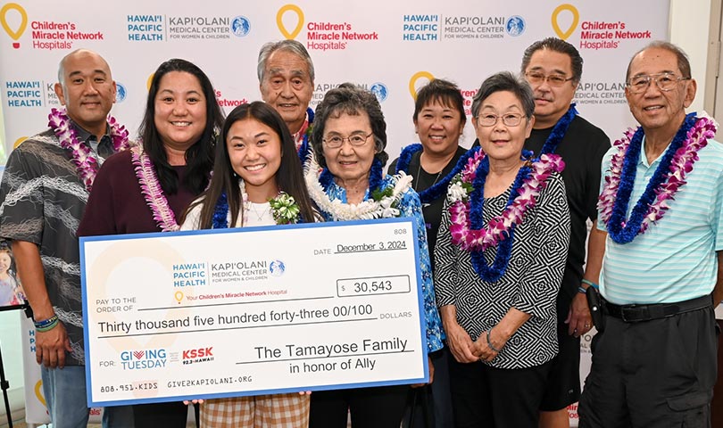 Smiling family group wearing lei and holding a giant check.