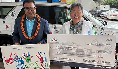 Two men in front of a Hyundai, one holding a sign with children's hand prints, the other in a white coat holding a giant check.