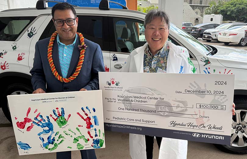 Two men in front of a Hyundai, one holding a sign with children's hand prints, the other in a white coat holding a giant check.