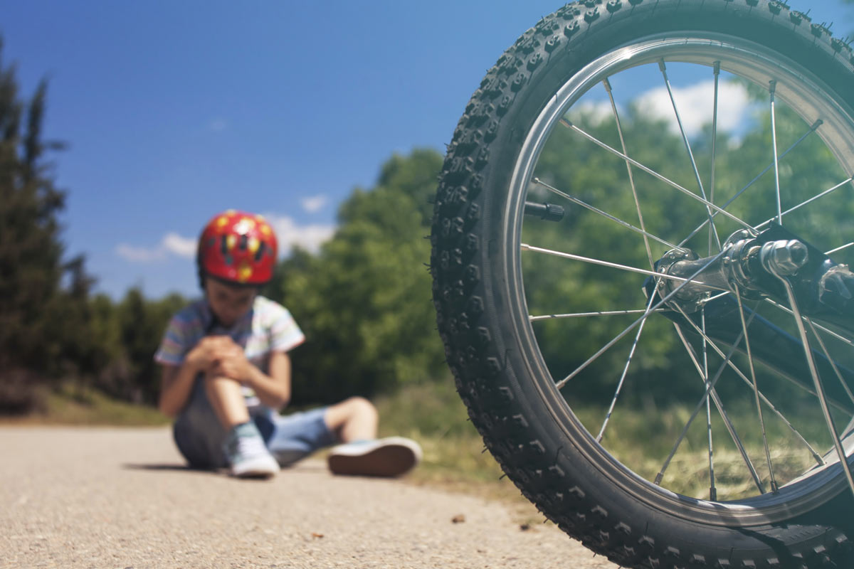 child sits on the side of the road holding knee in pain after an e-bike accident