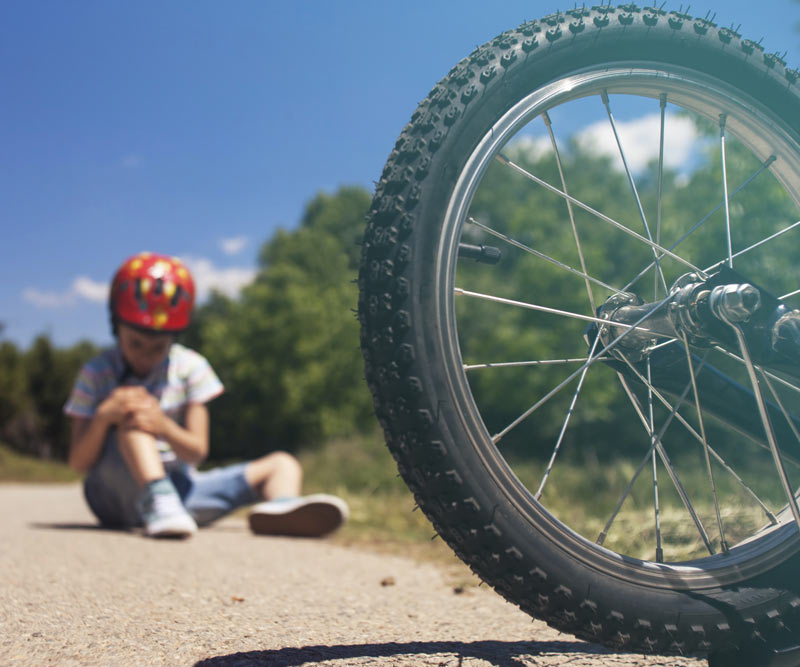 child sits on the side of the road holding knee in pain after an e-bike accident