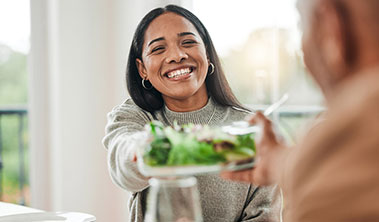 Smiling woman reaching across table with a plate of green salad.