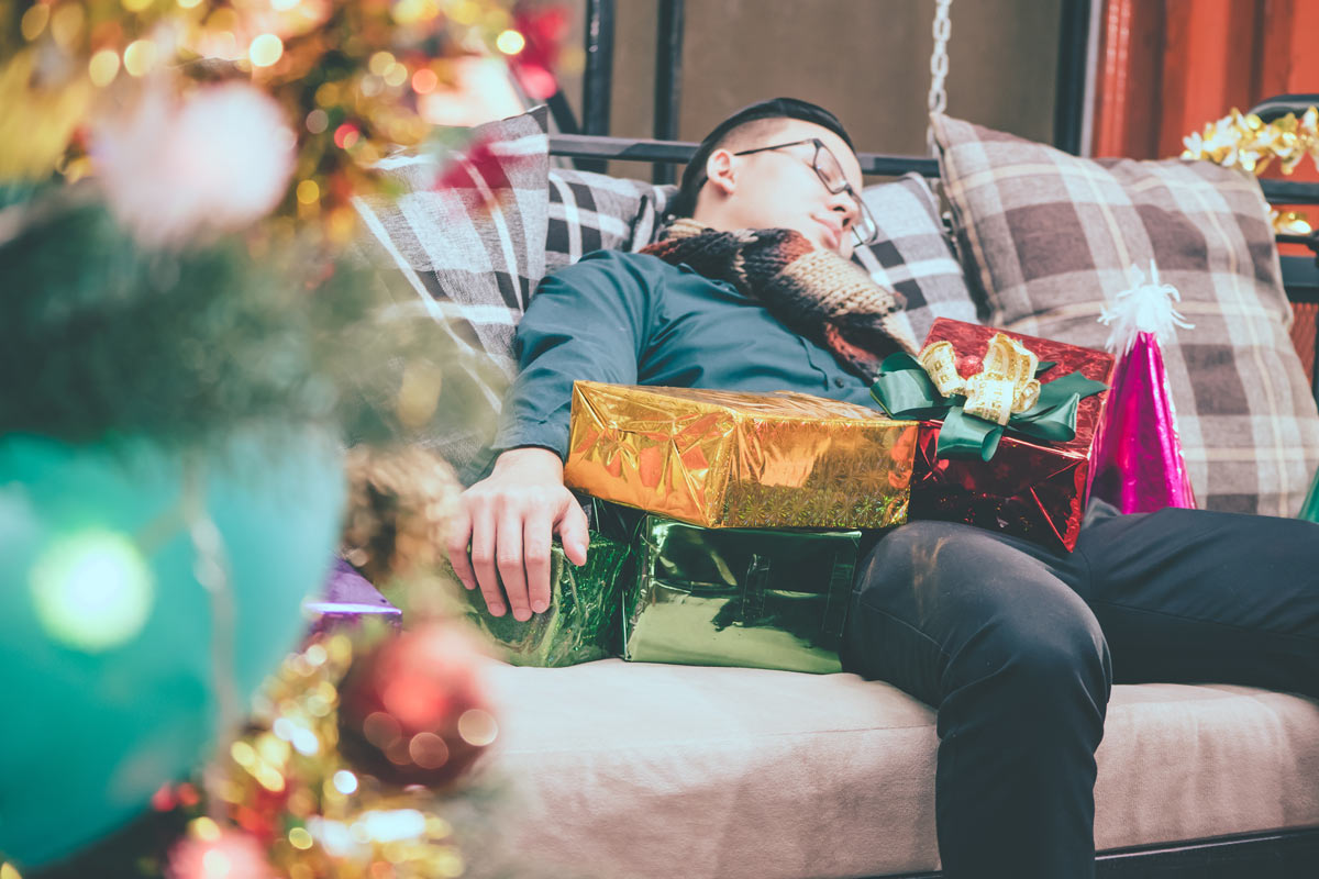 man asleep on couch surrounded by Christmas presents