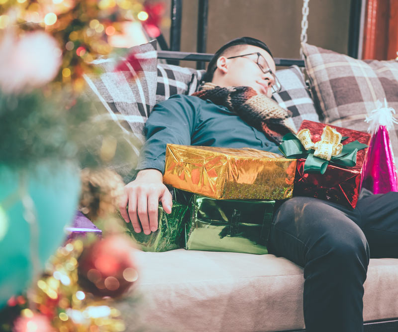 man asleep on couch surrounded by Christmas presents