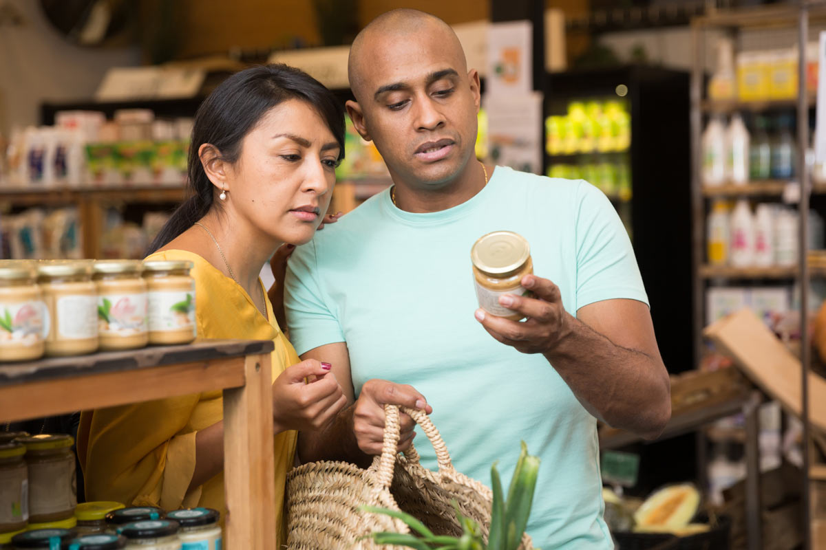 a man and woman look at a label on a jar of honey in a grocery store