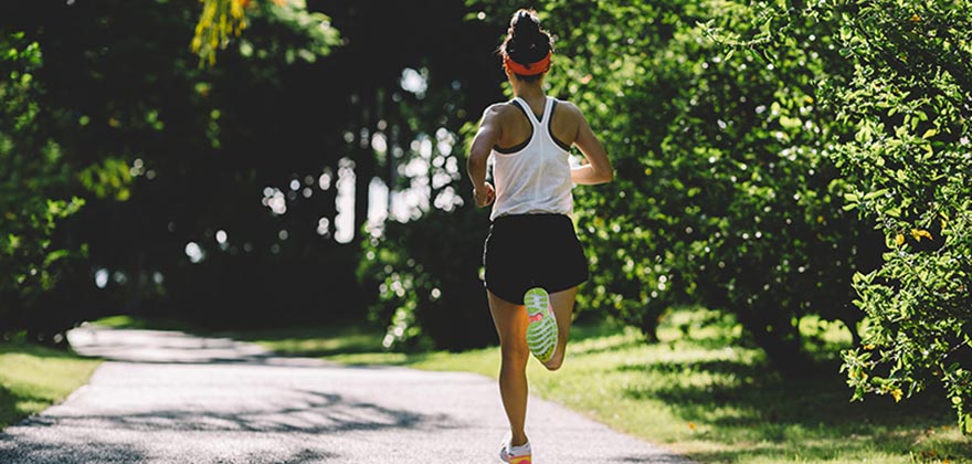 Solo runner on a paved path surrounded by greenery.