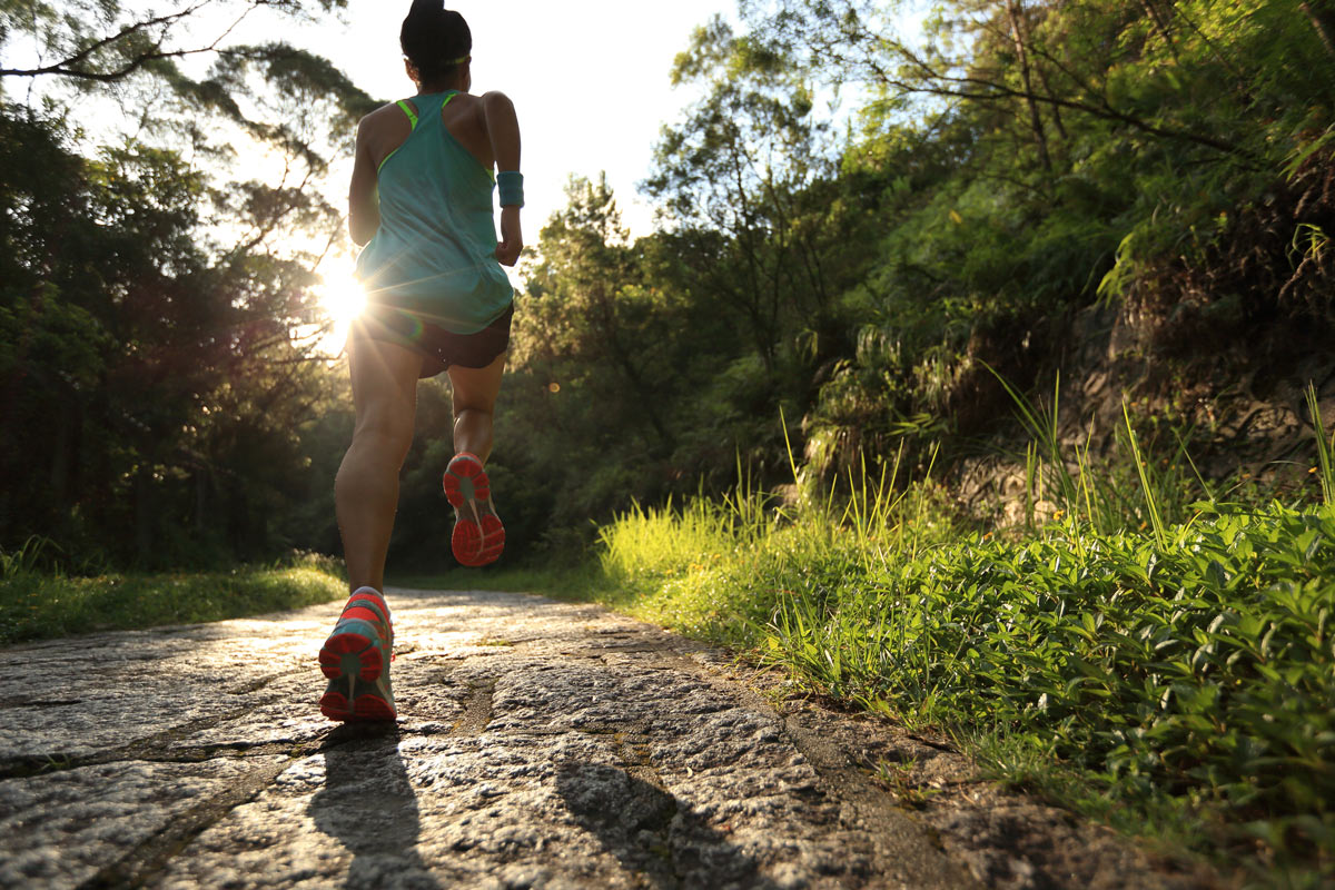 A female runner runs uphill on an open forest trail