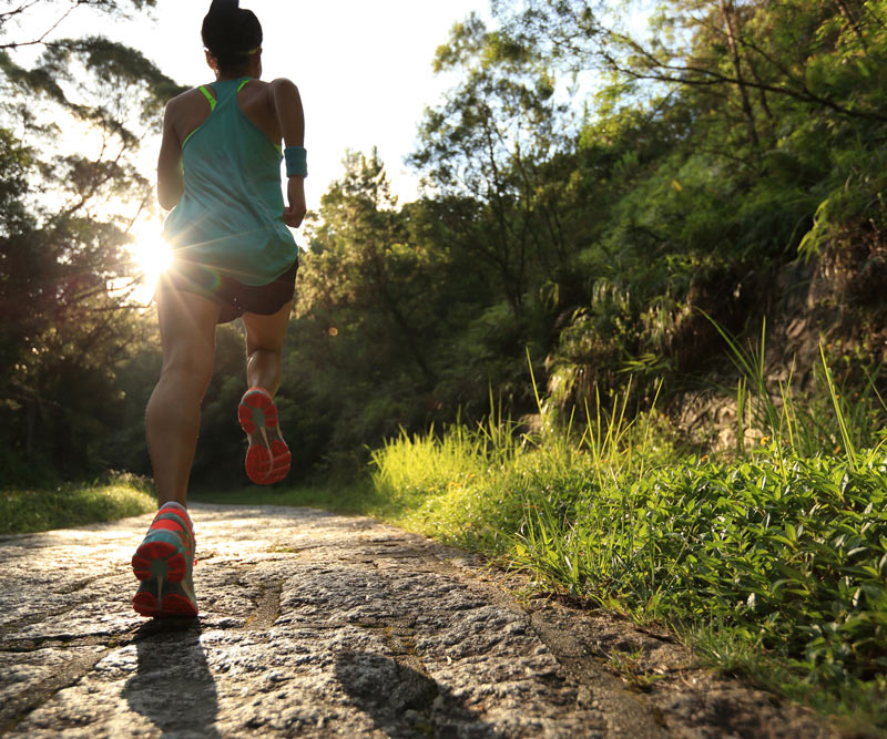 A female runner runs uphill on an open forest trail