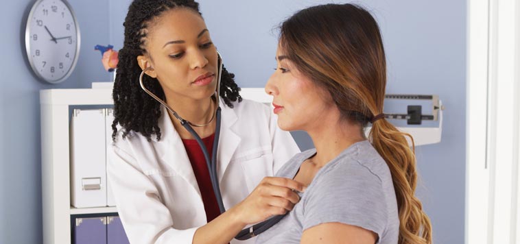 woman doctor listens to heartbeat of woman patient in an exam room