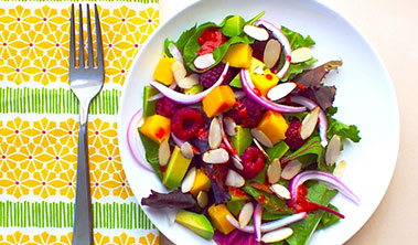 Colorful place setting with a fresh and healthy salad made with raspberries avocado and mango.