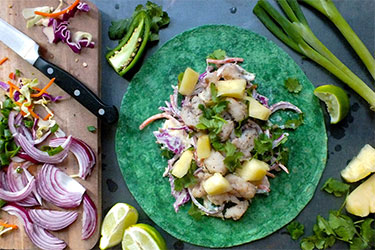 Green tortilla piled with fish and other fillings.