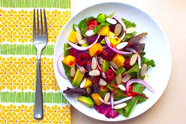 Colorful table setting featuring healthy salad with raspberry avocado and mango.