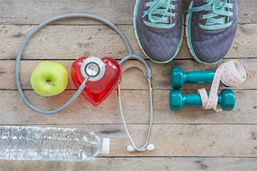 Photo collage with running shoes, water, an apple, small hand weights, a heart and a stethoscope.