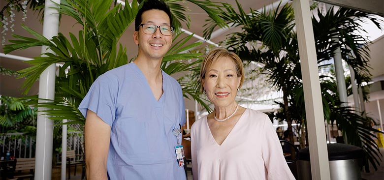 Younger male doctor standing beside older female patient.