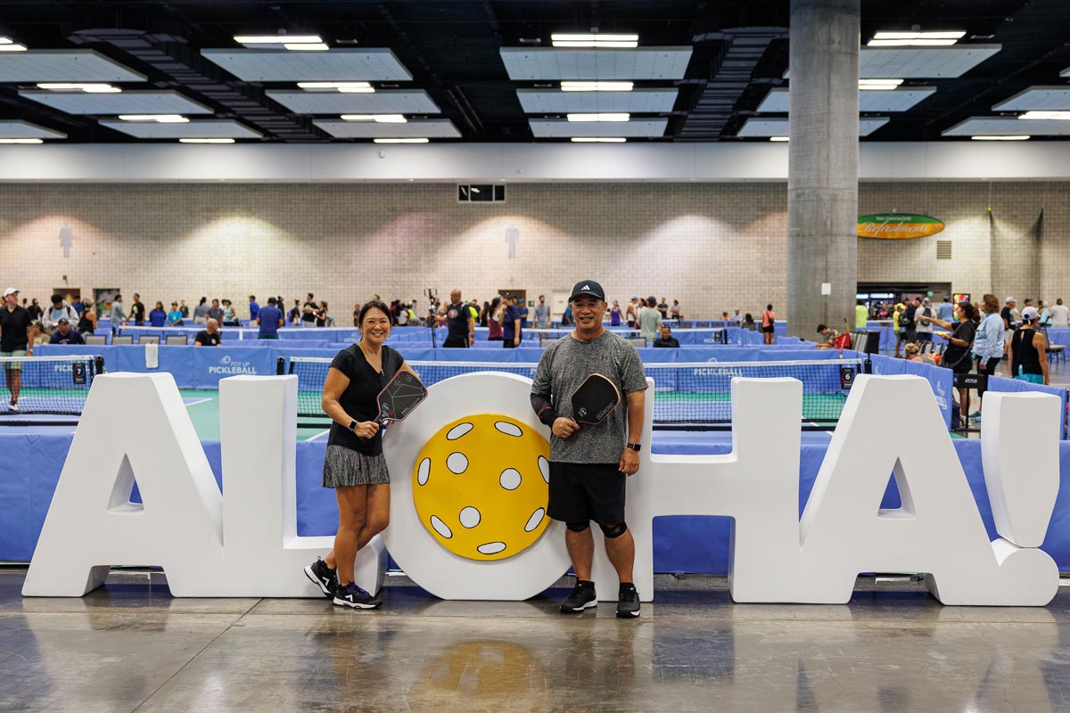 two pickleball players stand in front of a giant ALOHA sign