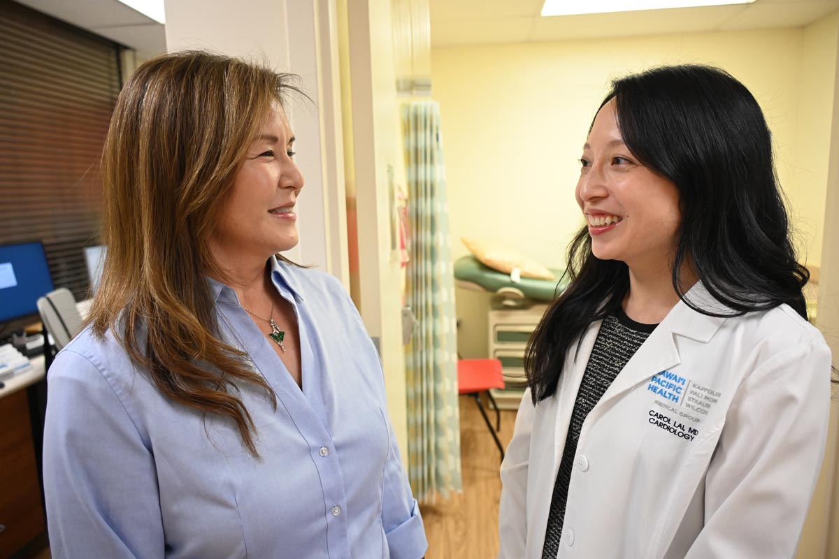 a female doctor and nurse talk to each other in front of an exam room in a clinic