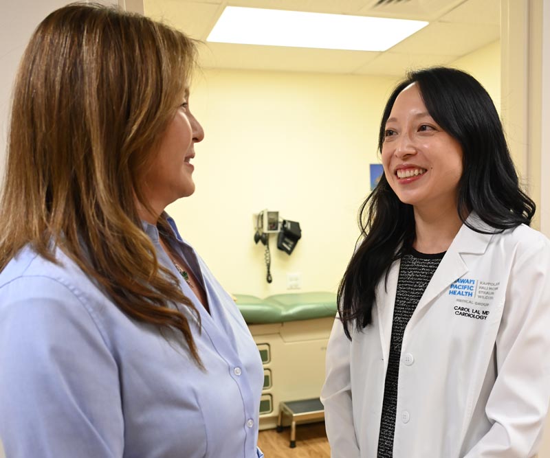 a female doctor and nurse talk to each other in front of an exam room in a clinic