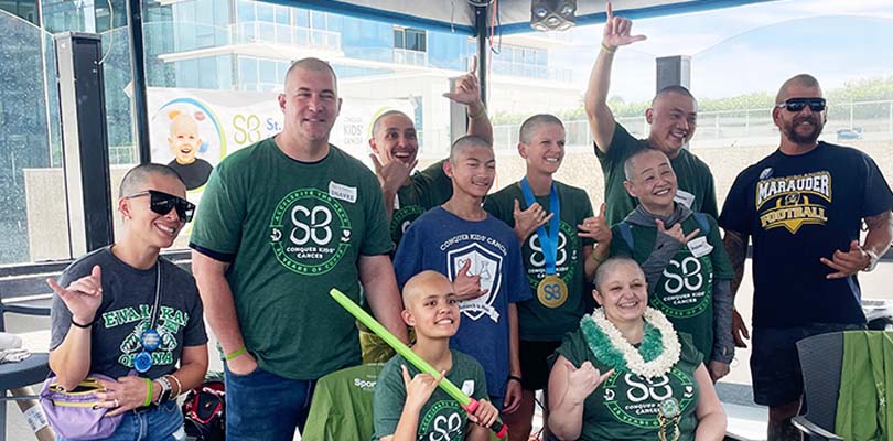 Group of shaved-head people in support of cancer research and kids battling cancer.