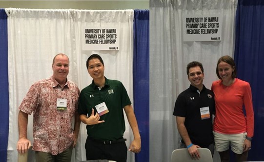 Two males standing next to sign and male and female standing next to sign